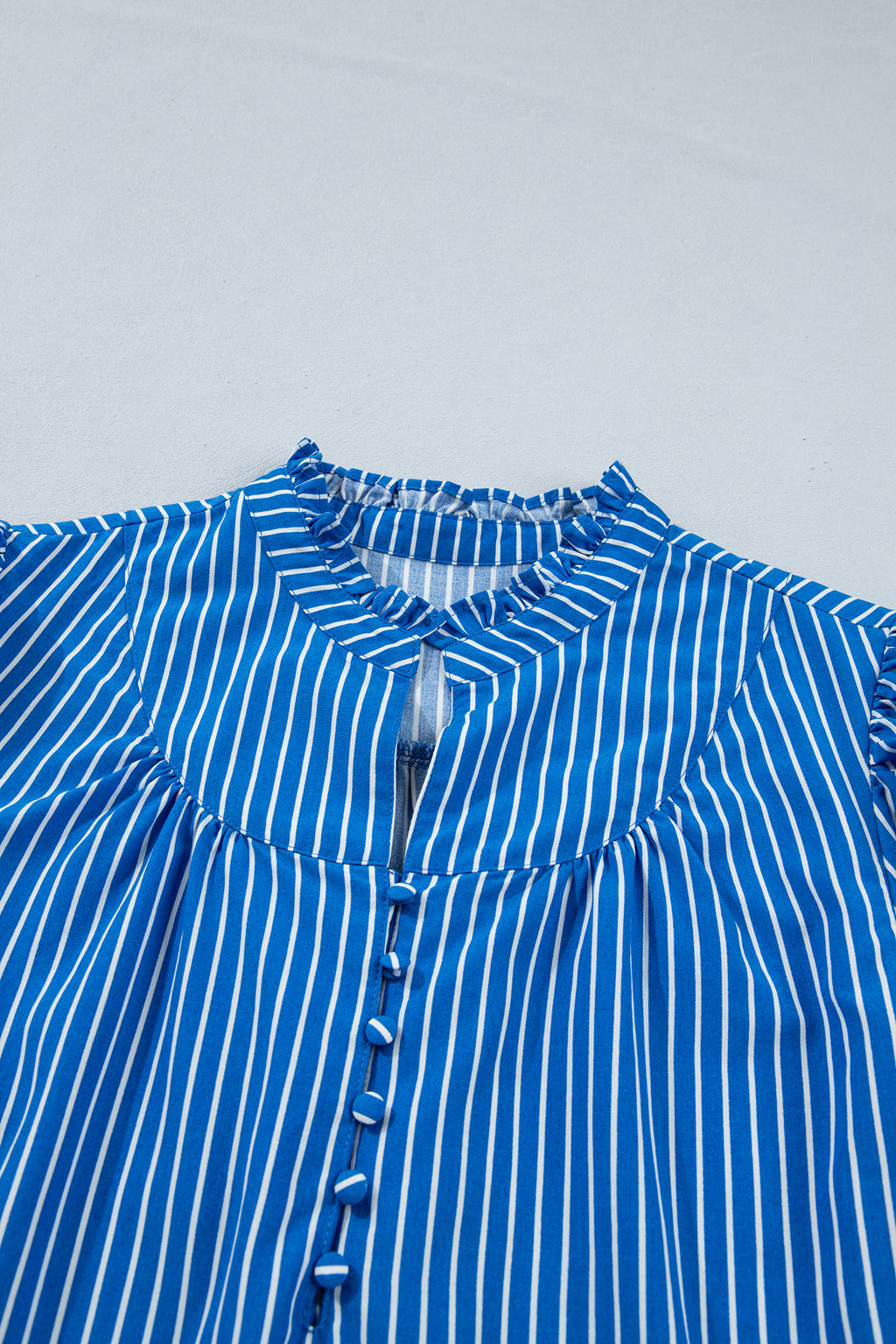 Blusa de manga corta abullonada con volantes y rayas azules, con botones en la parte delantera.