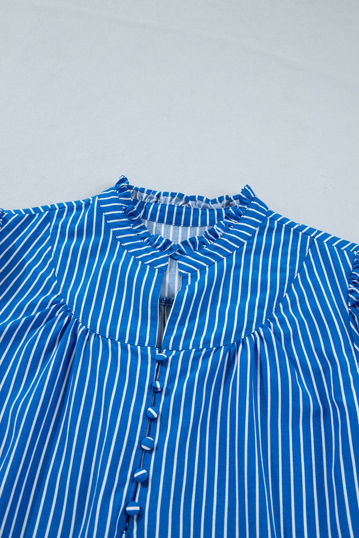 Blusa de manga corta abullonada con volantes y rayas azules, con botones en la parte delantera.