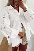 Camisa blanca con mangas abullonadas, bordado floral y detalles de ojales.